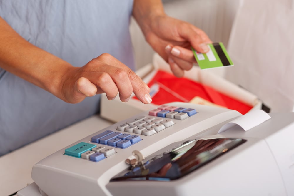 Midsection of saleswoman holding credit card while using ETR machine at boutique counter